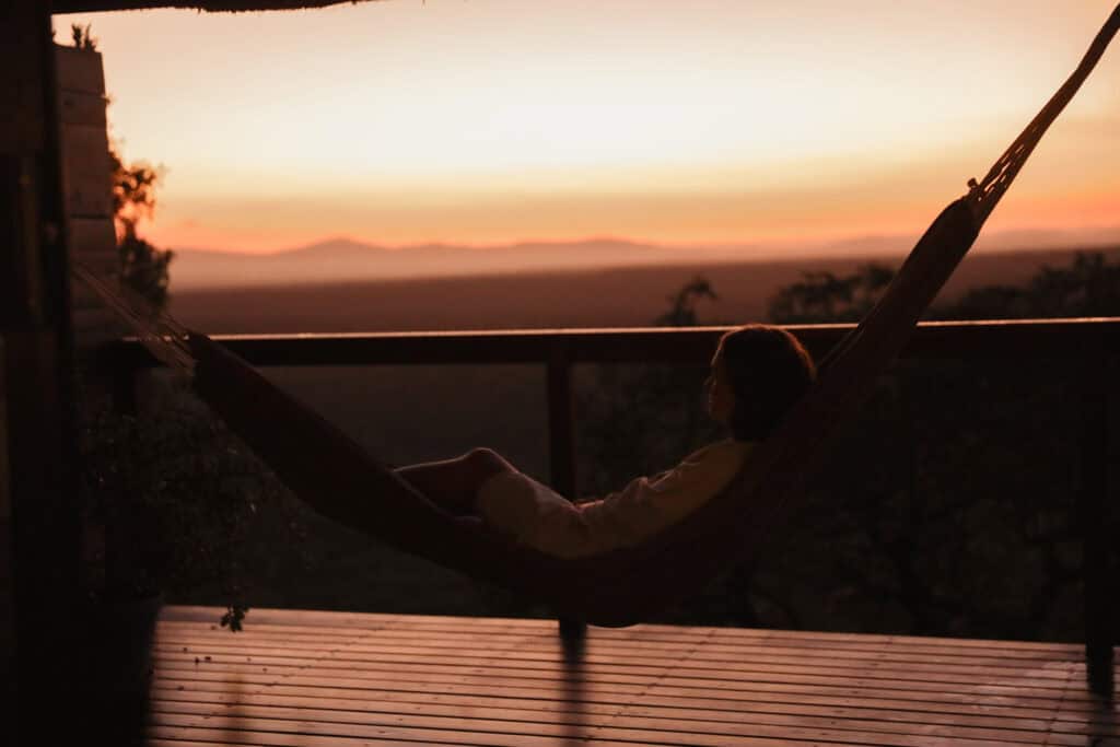 A guest relaxing in a hammock on a private wooden deck at Leopard Mountain Safari Lodge watching a golden bushveld sunset.