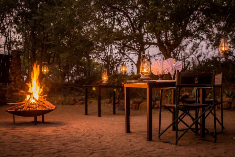 An open-air boma dinner set up around a crackling campfire with lanterns at dusk, highlighting the best time to visit south africa for a safari evening experience at Leopard Mountain